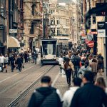 Bustling street scene in Amsterdam featuring a tram, shops, and diverse pedestrians on a lively day. Photo source: Metehan Demirkaya / Pexels.