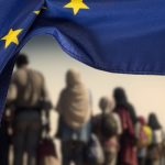 Flag of the European Union EU and a group of migrants (Photo: Bartolomiej Pietrzyk)