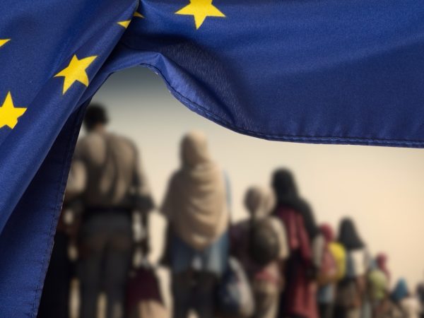 Flag of the European Union EU and a group of migrants (Photo: Bartolomiej Pietrzyk)
