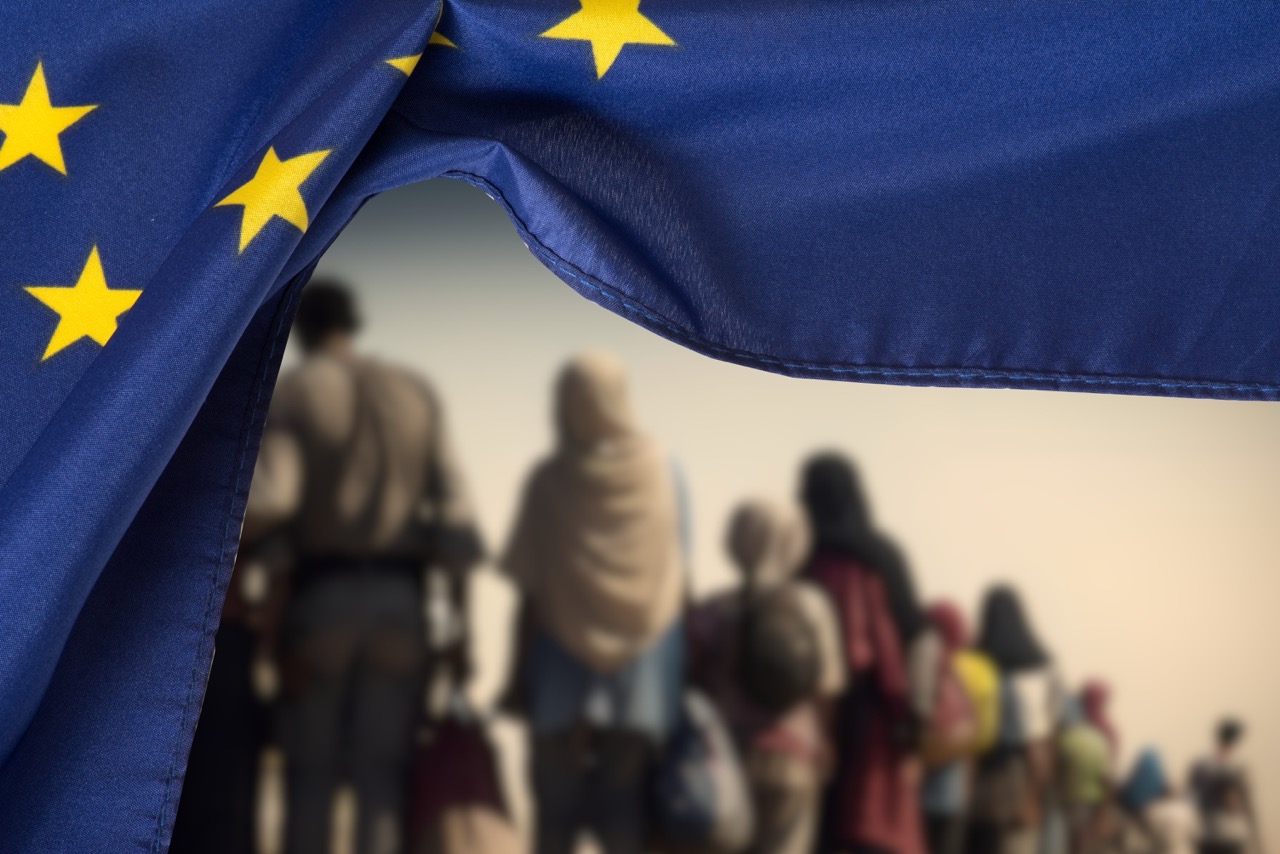 Flag of the European Union EU and a group of migrants (Photo: Bartolomiej Pietrzyk)
